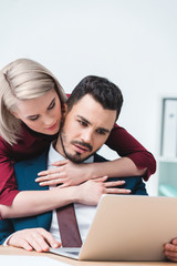 young woman hugging handsome businessman using laptop in office
