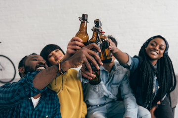 Naklejka premium smiling multicultural friends clinking bottles of beer