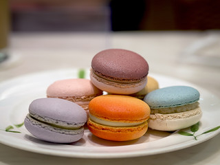 Close up of colorful French method macarons in white disk on white marble table in pastry shop