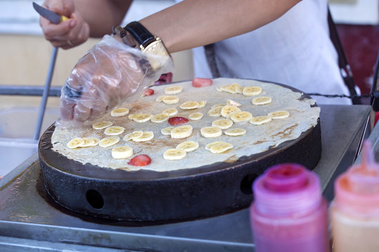Young male cook hand circles a thin pancake dough on professional pancake making cookware. Yummy food preparation in a street stand, culinary art restaurant or at home