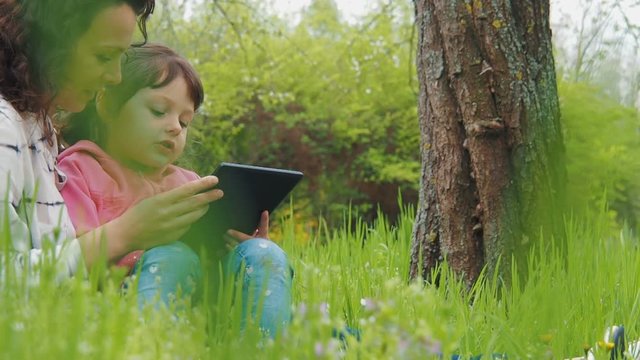 Family with a tablet in the park. A child with mother on the grass with a tablet.