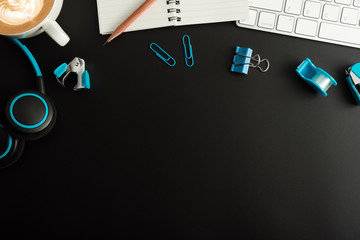 Flat lay, top view office table desk. Workspace with blank note book, keyboard, office supplies  and coffee cup on black background.