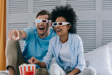 Laughing couple in anaglyph glasses watching movie at home with popcorn