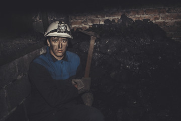 a miner with a pick sitting on the corner all tired and dirty from the coal dust after a hard work...