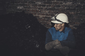a miner with a pick sitting on the corner all tired and dirty from the coal dust after a hard work in the mine