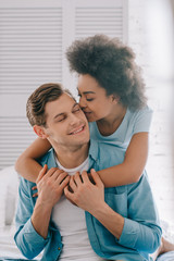 African american girlfriend embracing and kissing man sitting on bed