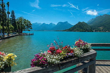 Pier with flowers on the Annecy Lake with blue sky mountains landscape. Near the lovely village of Talloires. Department of Haute-Savoie, southeastern France. 