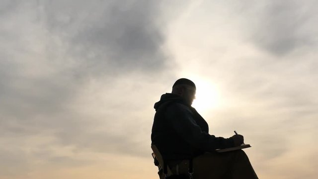 Man writing outdoors silhouette at sky background dolly shot