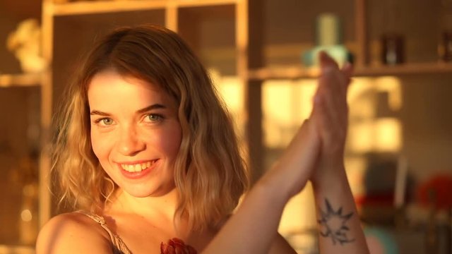 Beautiful young woman with blond hair standing in bright sunlight and clapping at camera.