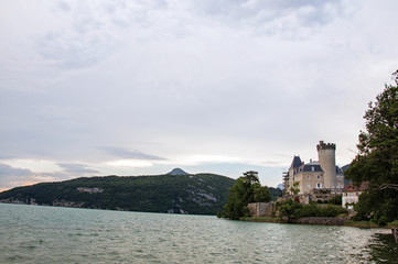 Naklejka na ściany i meble Duingt Castle with mountain landscape and cloudy sky next the Annecy Lake, near Annecy. Located at the department of Haute-Savoie, southeastern France.