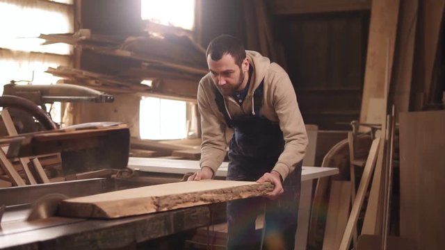 Caucasian man is working in his workshop. Concentrated sawing a wood on an electric machine