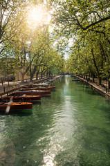 Fototapeta premium Large canal with boats and trees in the city center of Annecy. An historical and lovely lakeside town located at the department of Haute-Savoie, southeastern France. Retouched photo