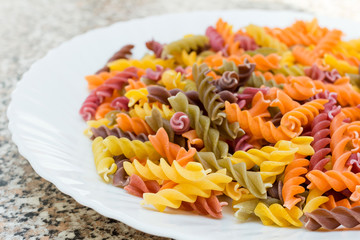 Fusilli pasta colored background. Classic Italian pasta in the form of a spiral of durum wheat. Raw pasta is put on a plate. Pasta from flour with additives of beets, carrots, cherries and spinach.