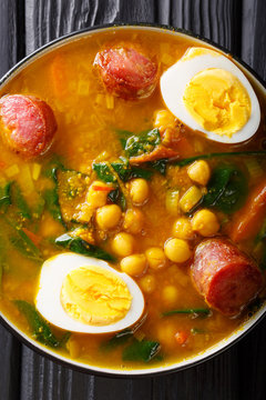 Spicy soup with spinach, chickpeas, chorizo sausages, boiled eggs close-up in a bowl. Vertical top view
