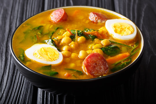 Traditional Spanish chickpeas with spinach, sausages chorizo, boiled eggs close-up in a bowl. horizontal