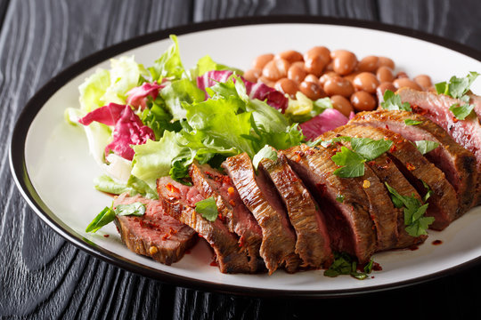Grilled chopped beef steak with fresh salad and beans close-up on a plate. horizontal