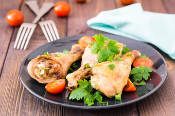 Baked chicken legs in spices with tomatoes and greens in a plate on a wooden table