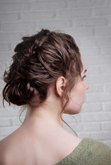 Hairstyle of a high bun on the head of a brown-haired close-up of a rear view against a white brick wall.