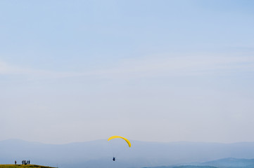 Paraglider flying over mountains in sunny summer day. Minimalism. Beautiful nature landscape. Group of hikers on top of rock.  Travel, tourism and leisure outdoor actvity on vacation. Freedom.