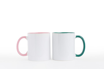 Two white mugs, with a green and pink handle on a light background. 