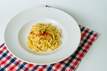 Italian cuisine, Fettuccine Carbonara with Bacon placed on white dish. A part of ingredient for this menu is eggs, hard cheese, guanciale, and pepper.