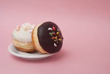 Doughnuts with Chocolate and White Icing on White Plate over Pastel Pink Background. Sweet Dessert Donuts with Copy Paste.