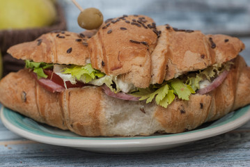 Croissant Sandwich with Tomatoes, Fresh Vegetables, Green Olive on Wooden Textured Grey Background. top view.