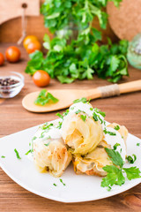 Appetizing ready-to-eat cabbage rolls with minced meat, sour cream and fresh herbs on a plate on a wooden table