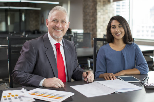 Portrait of smiling experienced mentor and young female employee. Mid adult man in formal jacket and Indian woman in casual wear posing at workplace. Business mentoring and teamwork concept