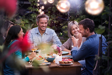 Group of friends gathered around a table in a garden on a summer evening to share a meal and have a good time together