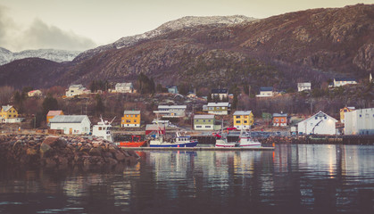 Fototapeta premium Harbor in a little fisherman village with moored boats and yachts with snow-capped peaks in the background.