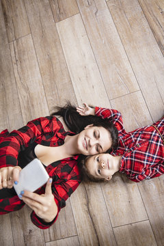 Beautiful happy family mother and daughter happy making selfie on mobile phone together at home lying floor top view