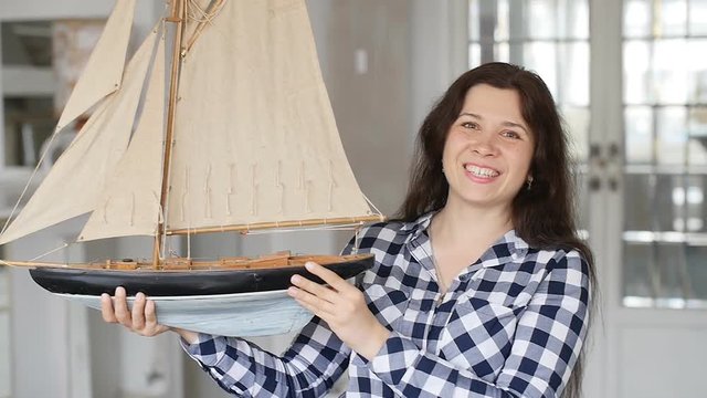 A happy young woman is holding a model of a sailing ship