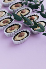 Composition of delicious praline sweets with almonds and green twigs on purple background