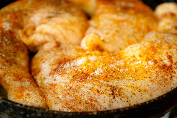 Raw chicken legs with spices on it. In a frying pan.