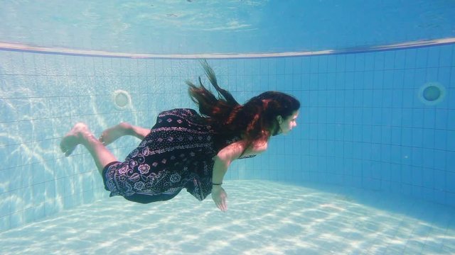 Young girl in dress dive in swimming pool