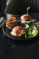 Delicious burgers with lettuce on black plate in cafe