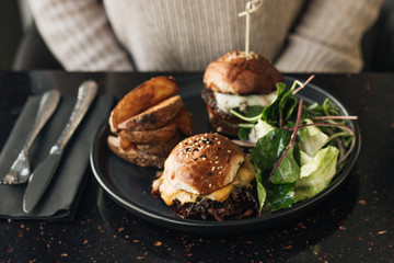 Delicious burgers with lettuce on black plate in cafe, woman sitting at the table