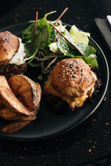 Delicious burgers with lettuce and fries on black plate in cafe