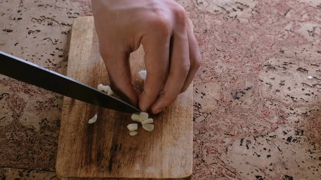 Man cuts garlic on slices on a wooden board. Close-up man's hands.