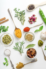 Fresh herbs and dried colorful spices in spoons and bowls arranged geometrically on white background