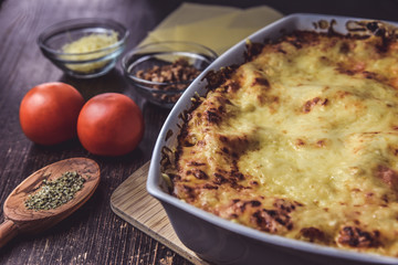 lasagne layered served on a wooden board with fresh tomatoes alongside