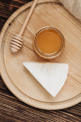 Honey dipper, delicious cheese piece and honey on wooden board