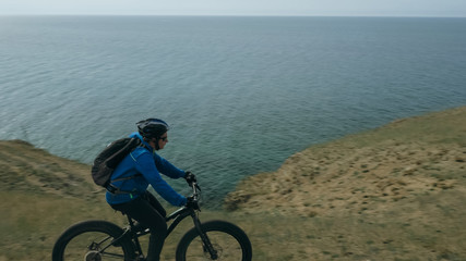 Fat bike also called fatbike or fat-tire bike in summer driving through the hills. The guy is riding a bike along the sand and grass high in the mountains. He performs some tricks and runs dangerously