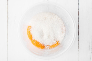 Cooking in the kitchen: egg yolks and sugar in a whisk can on a white wooden background, top view
