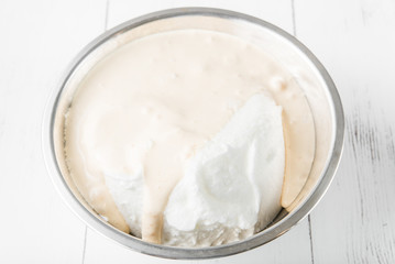 Cooking in the kitchen: egg yolks whipped with sugar mixed with whipped whites with one bowl on a white wooden background, top view