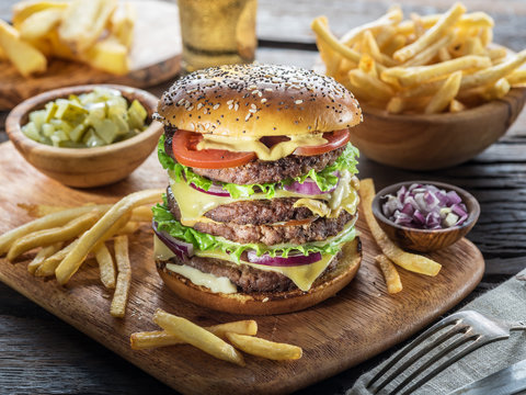 Big hamburger and French fries on the wooden tray.