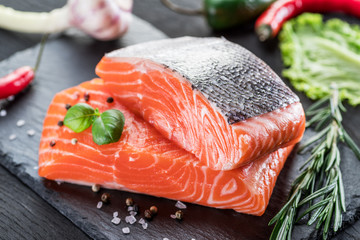 Fresh salmon fillets on black cutting board with herbs and spices.