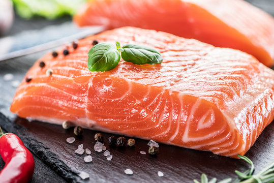 Fresh salmon fillets on black cutting board with herbs and spices.