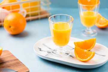 Glass of fresh orange juice with orange slices on white plate, blue background, cold summer refreshing nutritional beverage, blue orange color contrast, vitamin C healthy drink, copy space